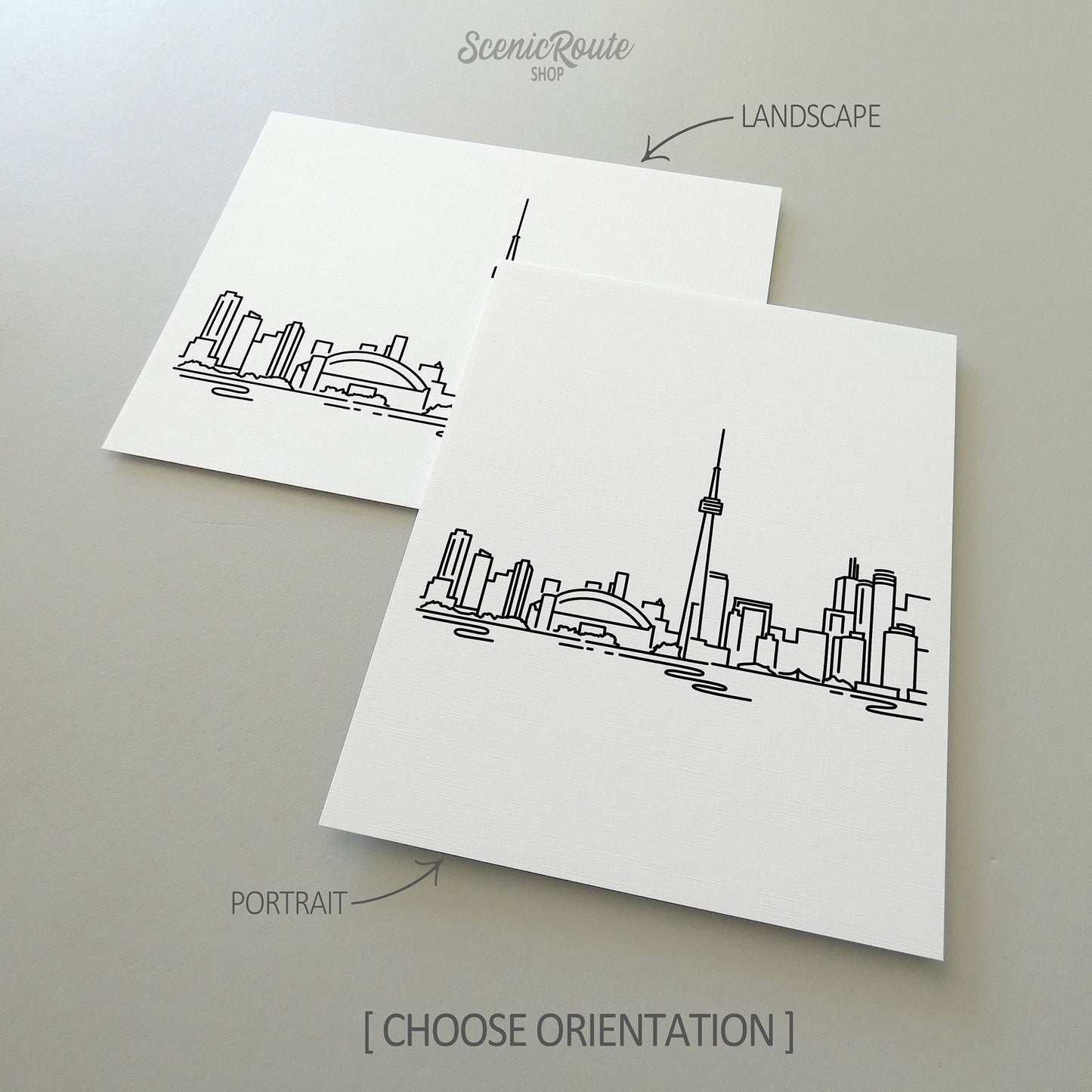 Two line art drawings of the Toronto Skyline on white linen paper with a gray background.  The pieces are shown in portrait and landscape orientation for the available art print options.
