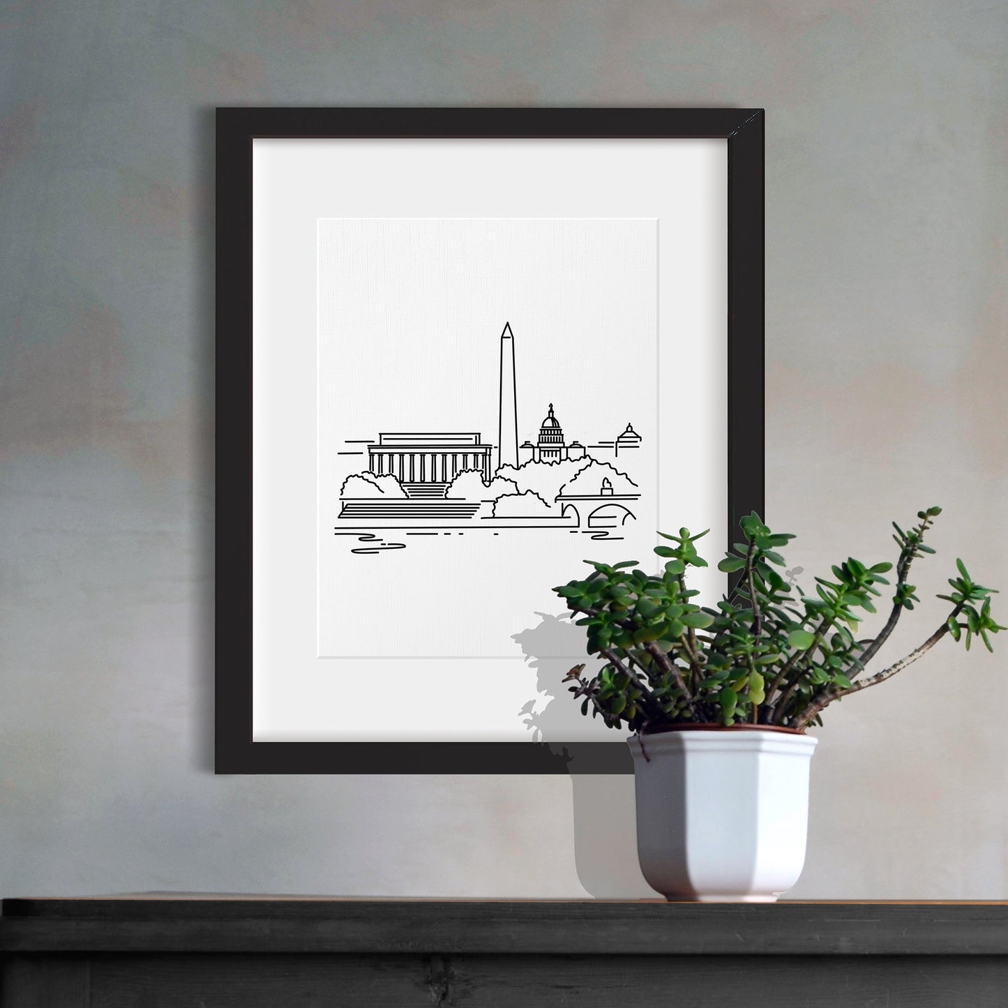 A framed line art drawing of the Washington DC Skyline hanging above a cabinet with a potted plant