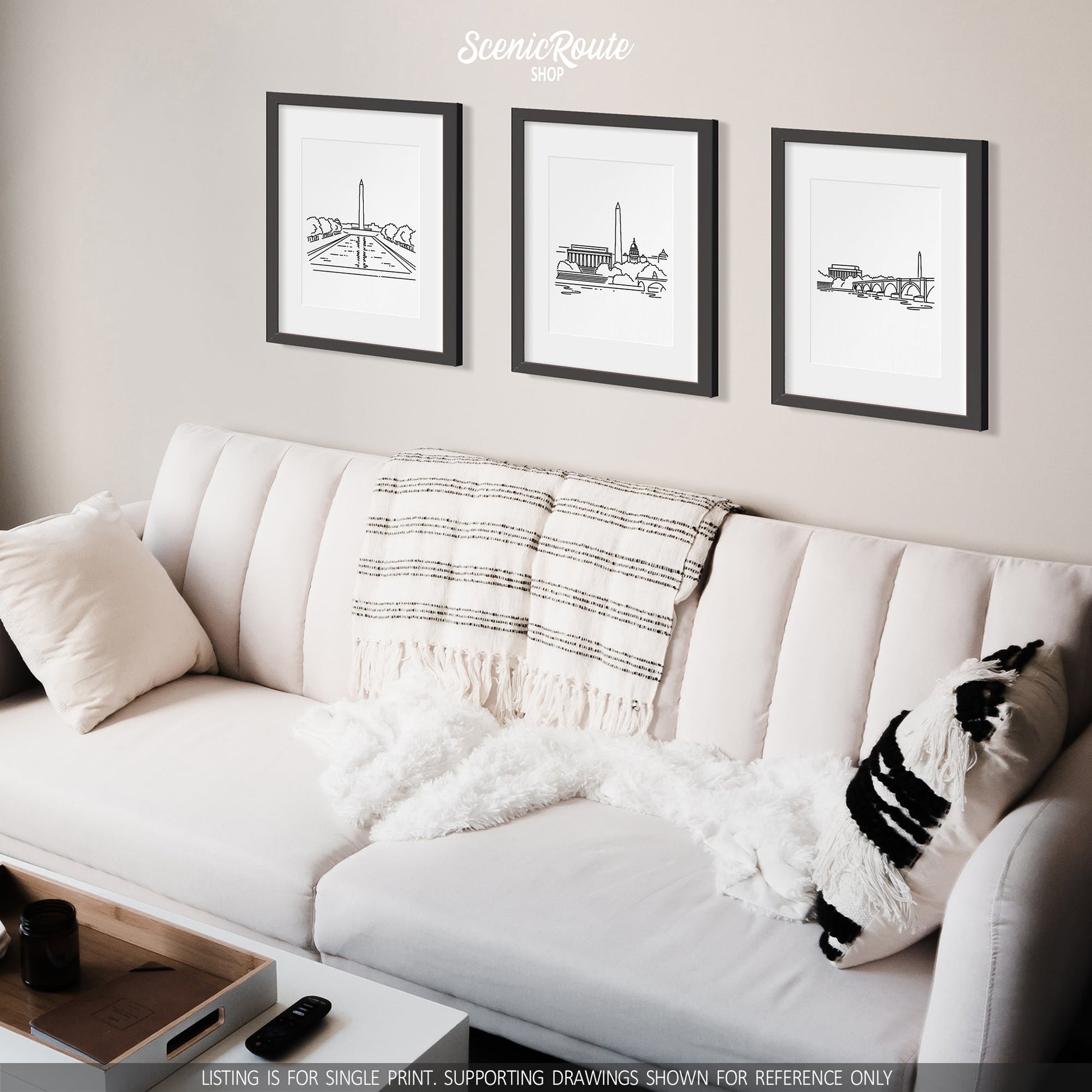 A group of three framed drawings on a white wall hanging above a couch with pillows and a blanket. The line art drawings include the National Mall, Washington DC Skyline, and Lincoln Memorial